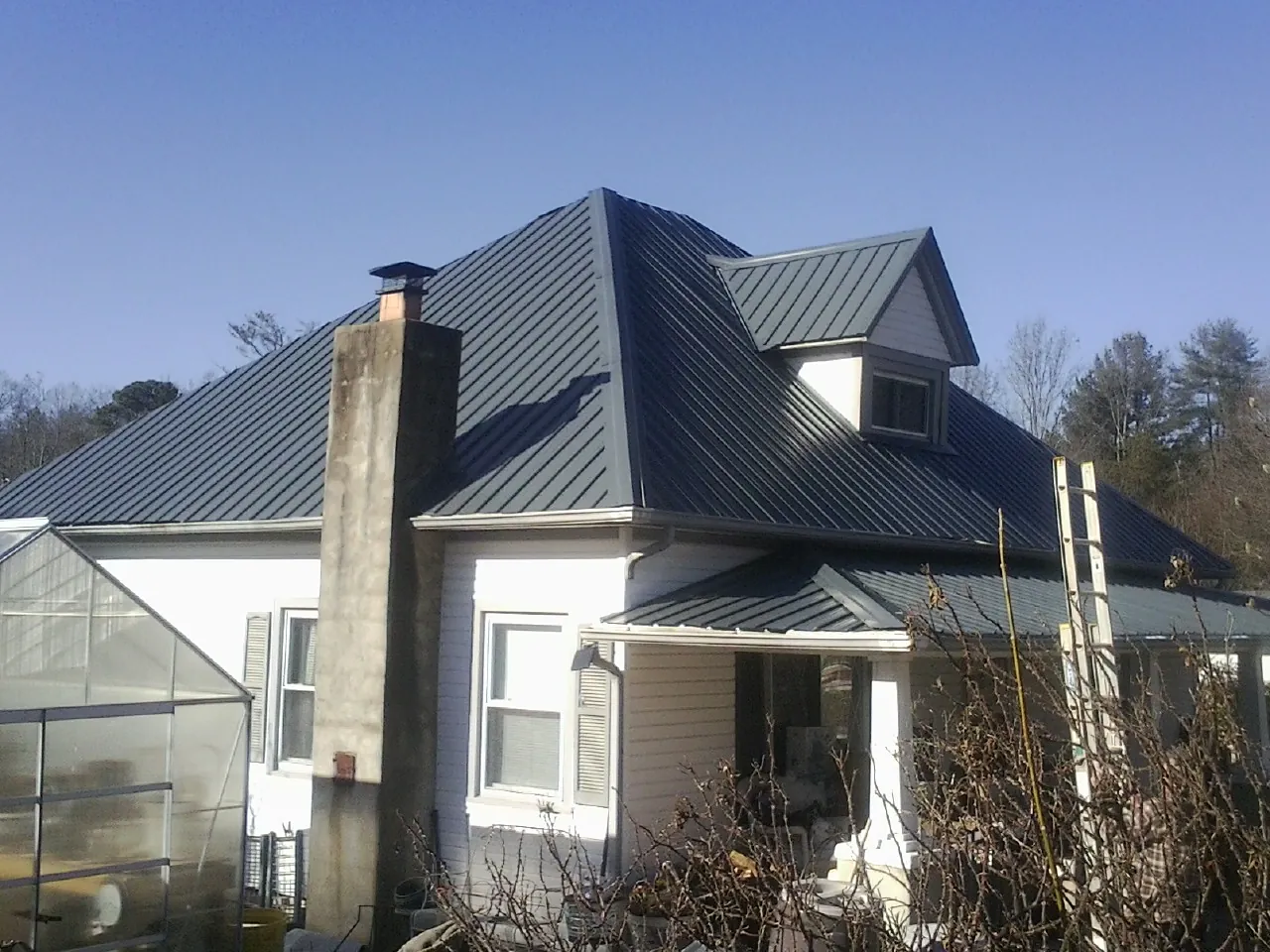 Dark blue standing seam metal roof on a white farmhouse with dormer — Slate & Tile Roof Repair by Roofing Brothers in Blue Mountain