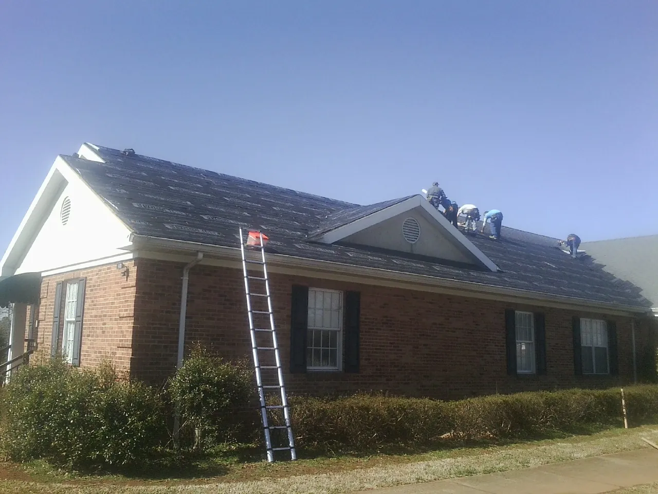 Crew tearing shingles off a brick ranch roof with a ladder set — Metal Roof Repair work by our crew in Blue Mountain