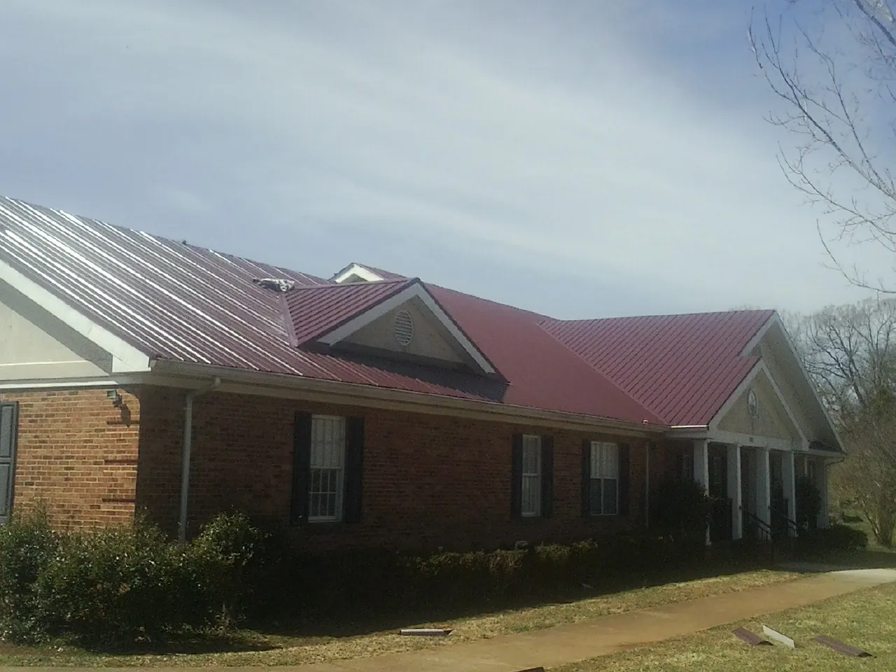 Red metal roof with gabled entries on a long brick building, from a Hail Damage Roof Repair job in Blue Mountain