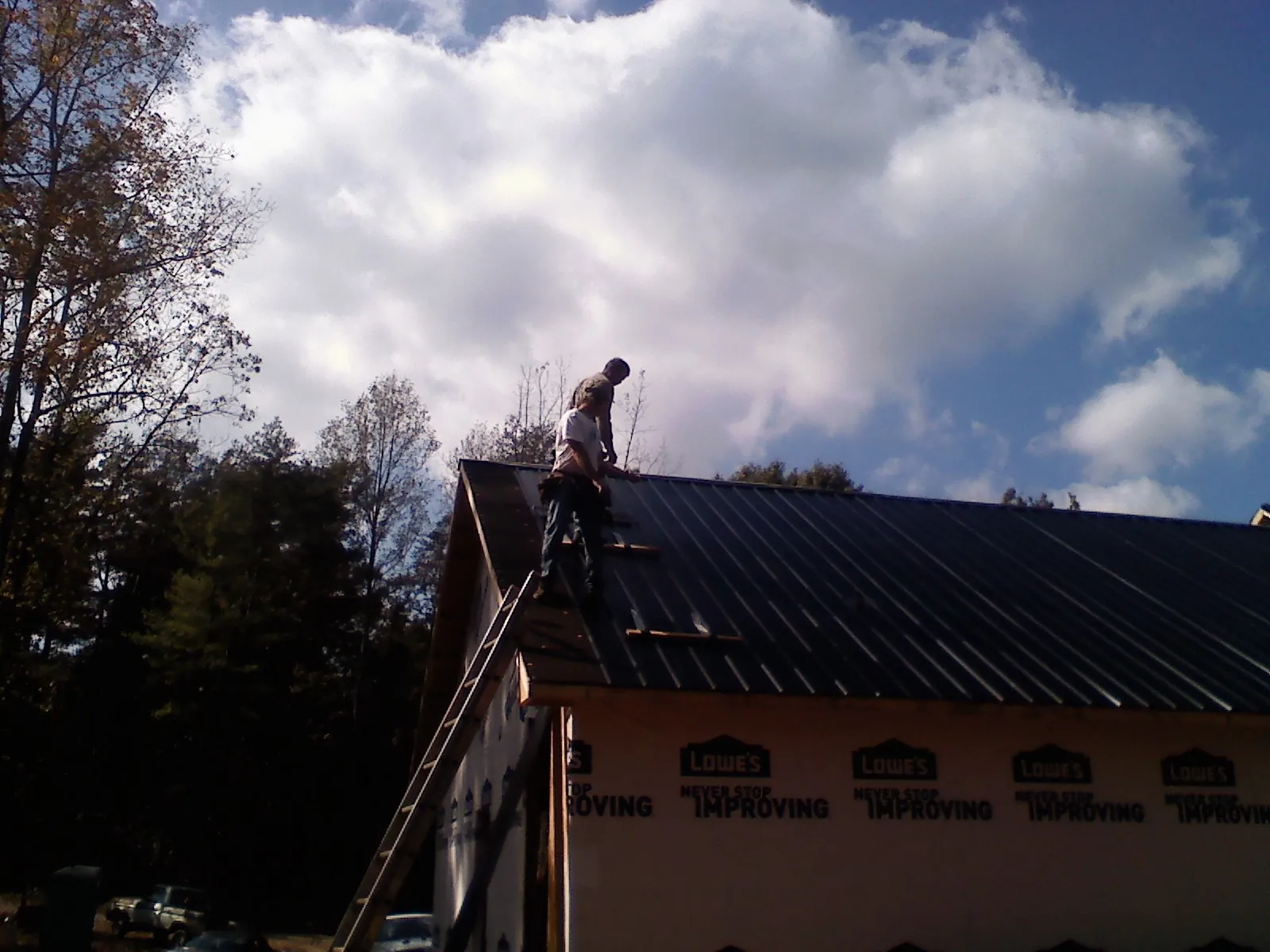 Roofer fastening dark metal panels high against a cloudy sky, from a Roof Inspection job in Blue Mountain