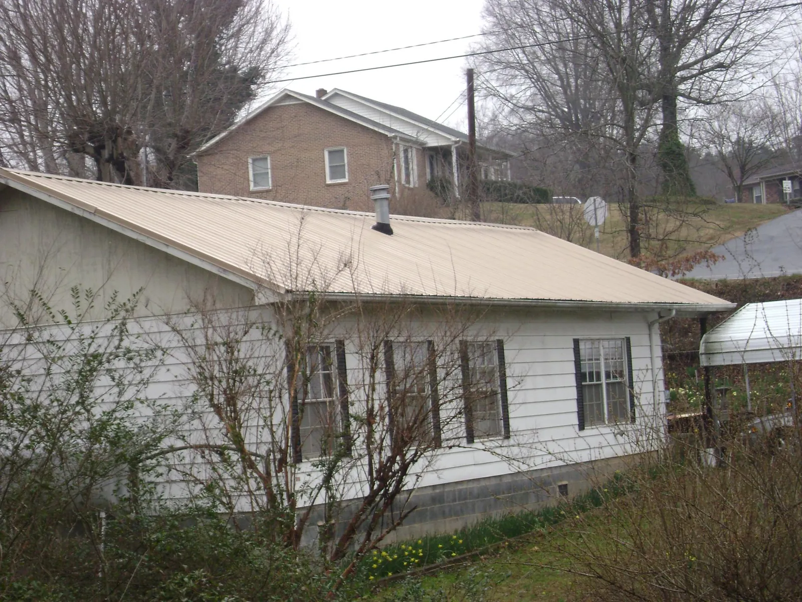 Tan metal roof on a white sided house set into a hillside — Commercial Roofing by Roofing Brothers in Blue Mountain