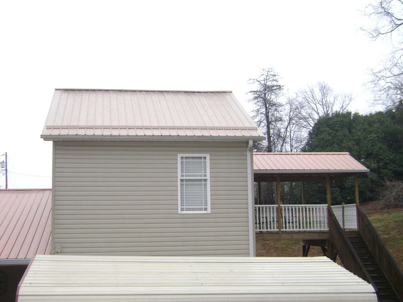 Tan metal roofs on a two story addition and attached porch, from a Roof Replacement job in Blue Mountain